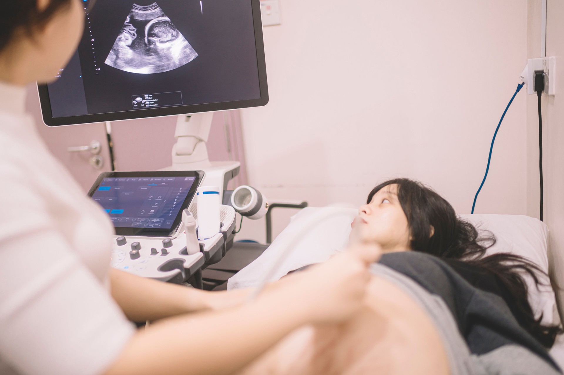 an asian chinese female Doctor perform Ultrasound / Sonogram Procedure to an asian chinese  Pregnant Woman. Obstetrician Moving Transducer on the Belly of the Future Mother